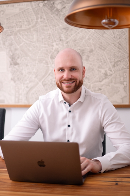 Versicherungsmakler Marcel Göbel sitzt am Tisch vor geöffnetem Laptop.
